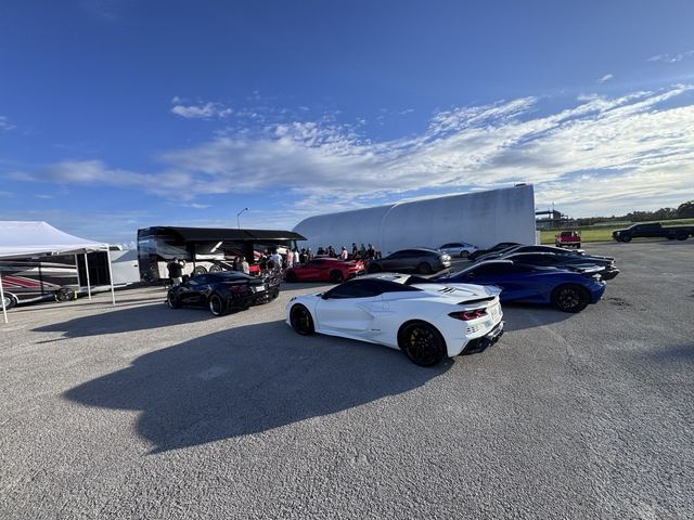 Sports cars displayed in the paddock with a transport trailer behind them.