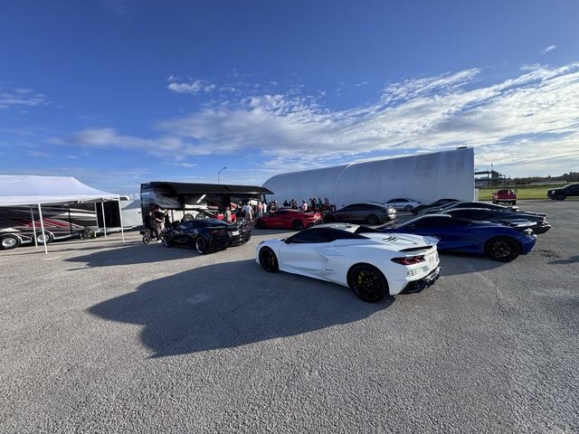 A white sports car parked in the paddock among other cars and trailers.