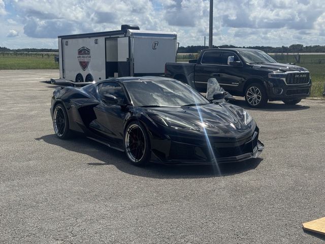A black sports car on the tarmac with a race trailer and pickup behind it.