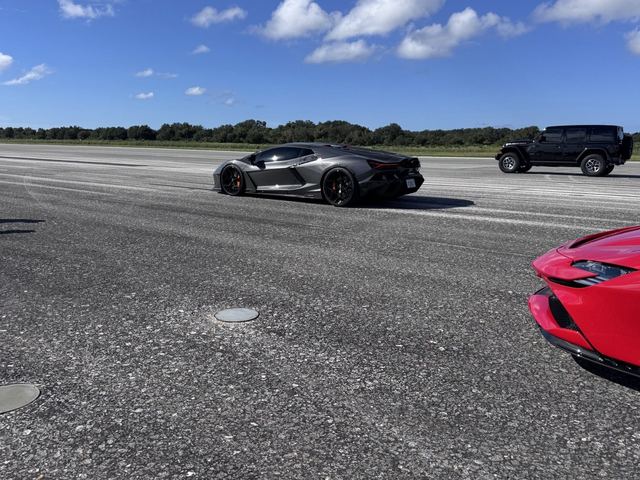 A silver sports car running down the runway with other cars in frame.