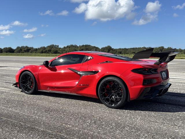 A red sports car with its hood open on the empty asphalt.