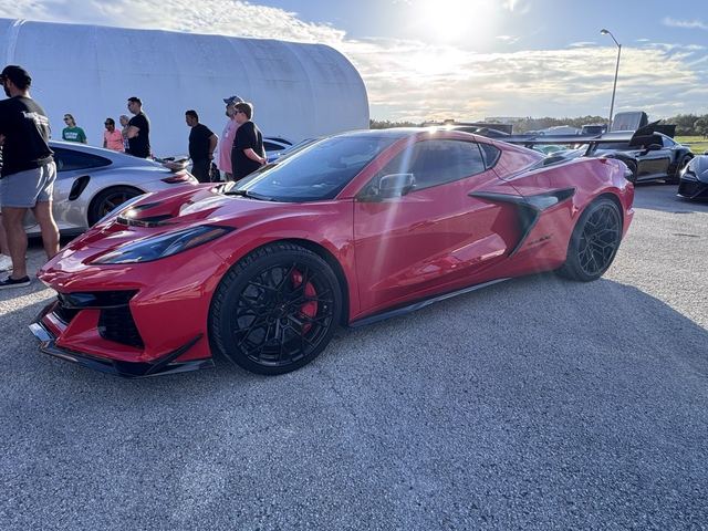 A red sports car on the asphalt with people standing behind it.