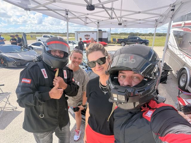 Drivers in helmets and gear posing with friends under the paddock canopy.