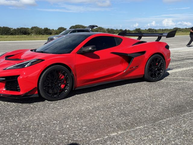 A red sports car with its door open on the concrete runway.