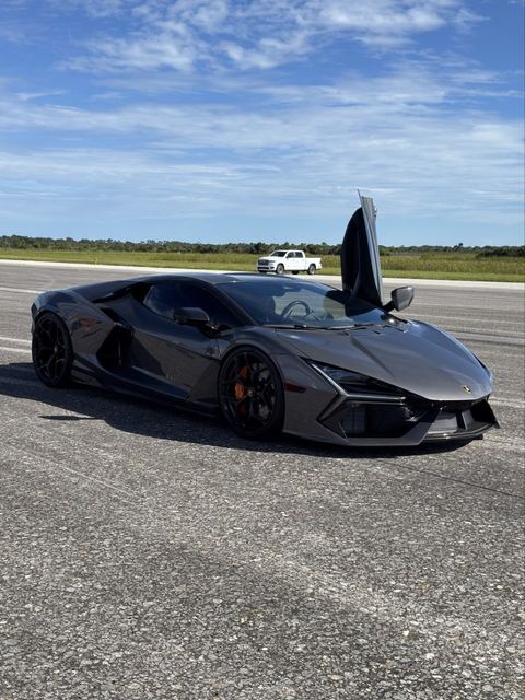 A dark gray supercar parked on the runway with its door open.