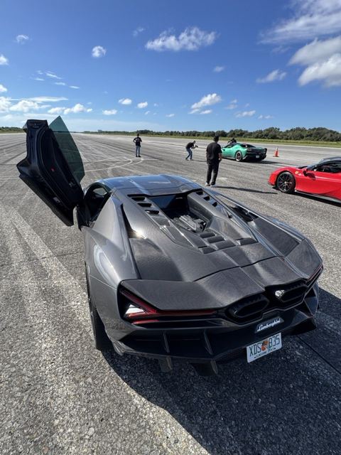 Rear view of a gray supercar with its scissor door open on the runway.