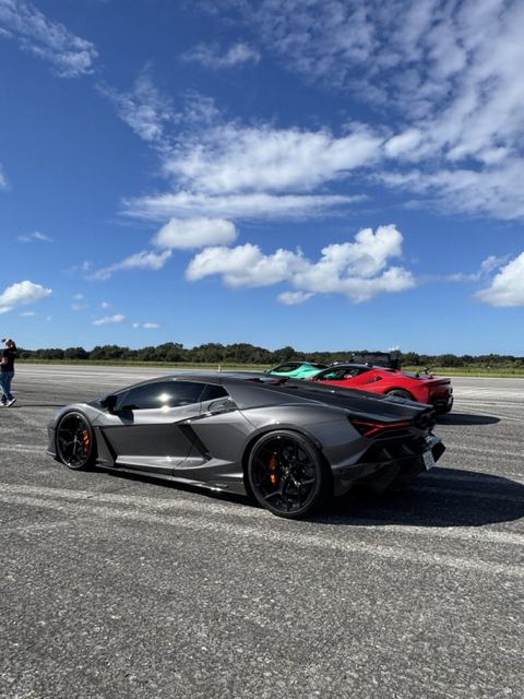 A dark gray sports car parked on the runway alongside other cars.