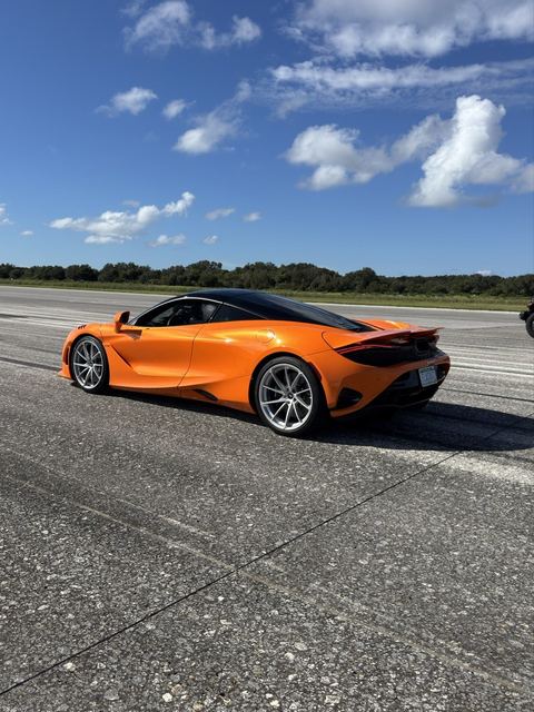 An orange sports car on the asphalt under a bright sky.