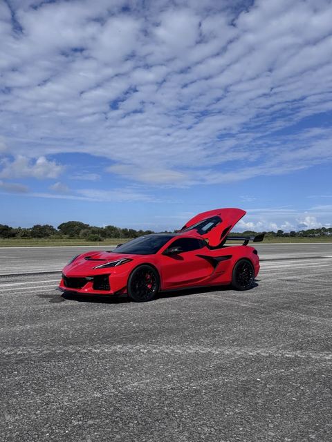 A red sports car with its hood raised on the runway.