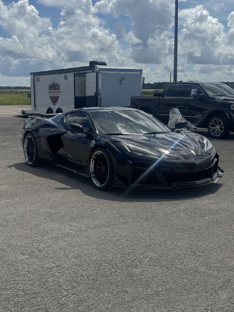 A black sports car on display with support vehicles behind it.