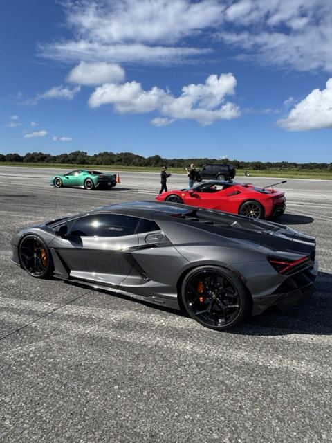 Three supercars on the concrete runway with crew and support vehicles behind.